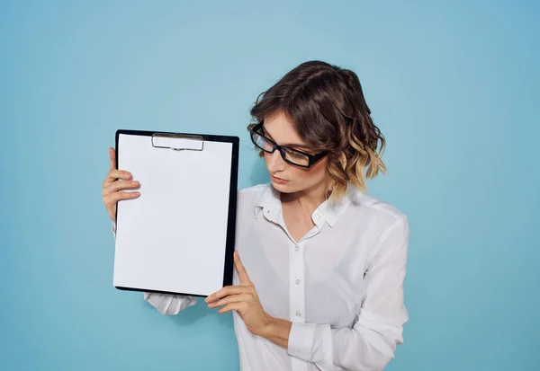 Un dossier avec une feuille de papier blanc dans les mains des femmes sur un fond bleu et des lunettes sur son visage — Photo