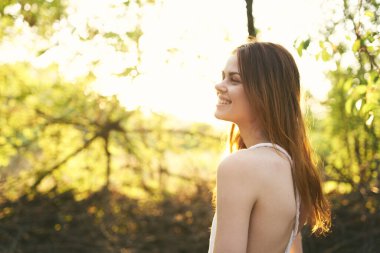 Mutlu kızıl saçlı kadın ormanda yeşil ağaçların yanında yaz güneşi