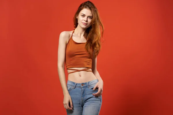 Mooie vrouw in rood t shirt en jeans straat mode aantrekkelijk look rood achtergrond — Stockfoto