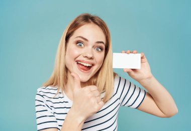 Mavi arka planda mutlu bir kadın elleri ve elinde bir kartvizitle el kol hareketi yapar.