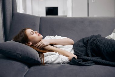 Evdeki kanepede uzanmış, boynunda sağlık sorunları olan bir kadın.