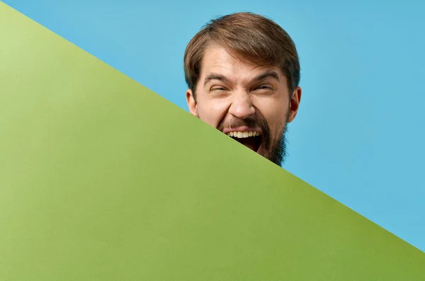 Эмоциональный бородатый мужчина выглядывает из-за зеленого баннера студия синий фон — стоковое фото