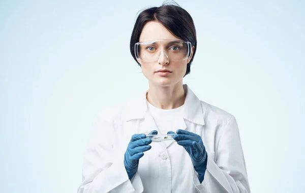 医療用のガウンと眼鏡の女性は植物を手にしたフラスコを持っています生物学植物医学 — ストック写真