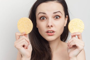 Çıplak omuzlu duygusal kadın, yüz estetiğine yakın süngerleri süngerliyor.