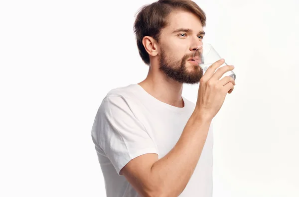 Schöner Mann trinkt Wasser aus einem Glas überrascht aussehen Emotionen weißer Hintergrund — Stockfoto