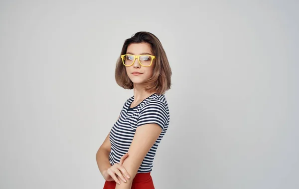 Retrato de uma mulher com óculos e uma camiseta listrada em um fundo cinza moda estilo saia vermelha — Fotografia de Stock