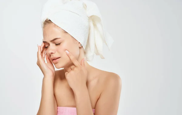 Mulher com uma toalha branca na cabeça toca seu rosto com as mãos em um fundo leve — Fotografia de Stock