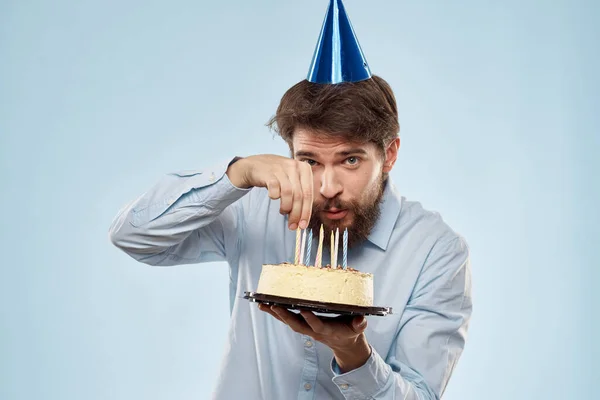 Pastel en un plato y hombre de cumpleaños con una gorra en su cabeza fondo azul — Foto de Stock