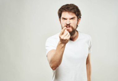 Beyaz tişörtlü öfkeli bir adam ellerini arka planda açık bir şekilde hareket ettiriyor.
