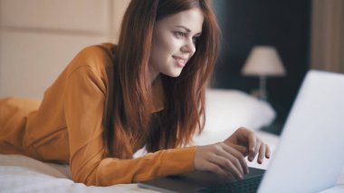 Yatakta dizüstü bilgisayarla internetten sohbet eden neşeli, güzel bir kadın.