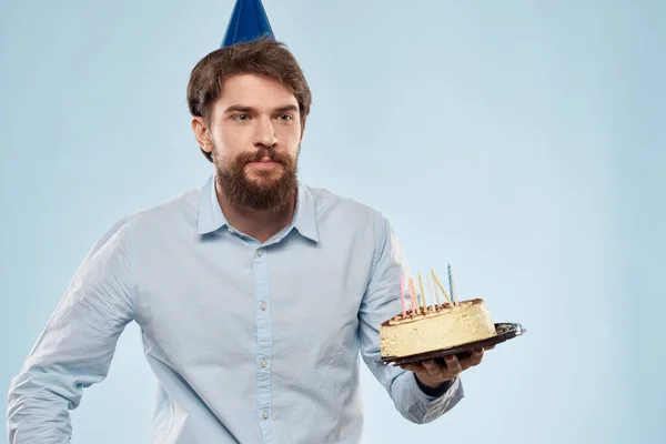 Pastel en un plato y hombre de cumpleaños con una gorra en su cabeza fondo azul — Foto de Stock