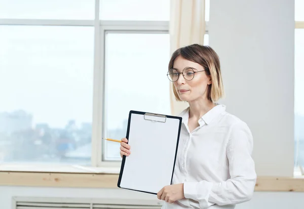 Une femme tient un dossier avec une feuille de papier blanche et une fenêtre en arrière-plan — Photo