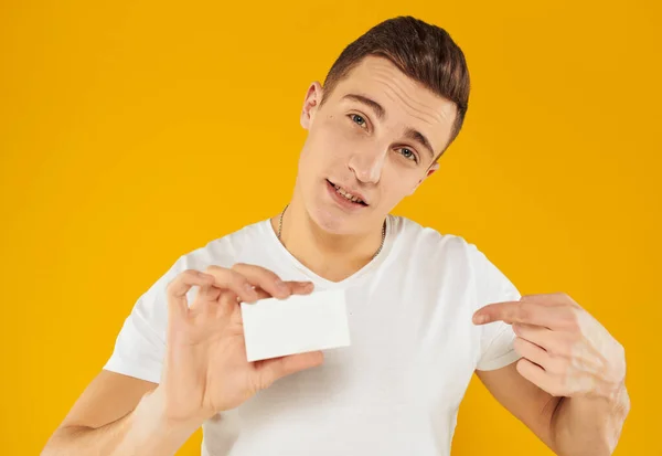 Hombre en camiseta blanca que muestra la tarjeta de crédito en el fondo amarillo vista recortada — Foto de Stock