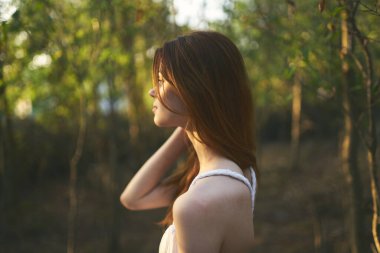 Bahçedeki ağaçların yanında bir kadın yaz tatili için beyaz elbise giyiyor.