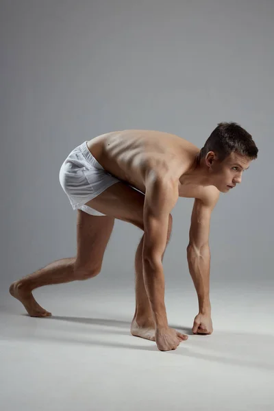 Atleta con un torso bombeado en pantalones cortos blancos sobre un fondo gris inclinado hacia adelante — Foto de Stock