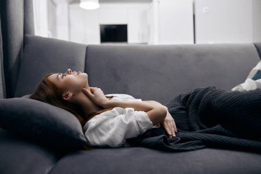 Bir kadın kanepede uzanır ve battaniyeli eli elleriyle kendini kötü hisseder.