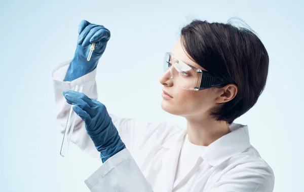 Kadın laboratuvar asistanı elinde cep şişesi, yüzünde gözlük ve tıbbi bir önlükle. — Stok fotoğraf