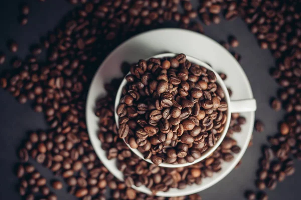 Granos de café en una taza y platillos blancos fondo gris de cerca — Foto de Stock