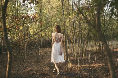Beyaz elbiseli bir kadın büyümüş olarak ormanda yürür.