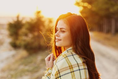 Ormanda gün batımında omuzlarında ekoseli kızıl saçlı bir kadın.