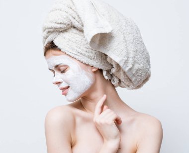 Kafasında havlu ve yüzünde siyah noktalar olan beyaz bir maske olan güzel bir kadın.