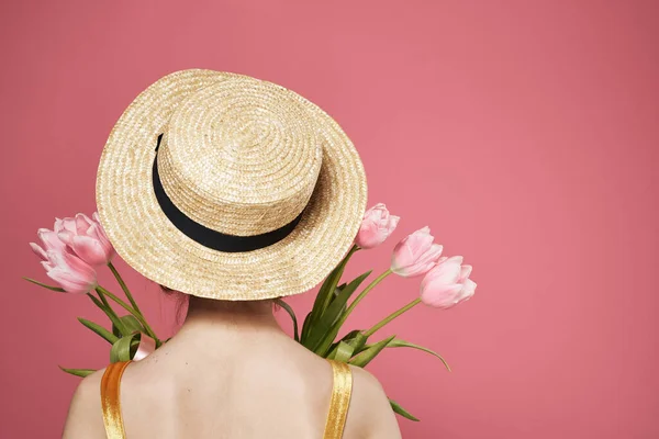 Mulher com chapéu de volta ver buquê de flores como um presente de fundo rosa — Fotografia de Stock