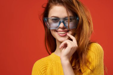 Sarı kazaklı bir kadın başını kırmızı arka planda tutuyor.