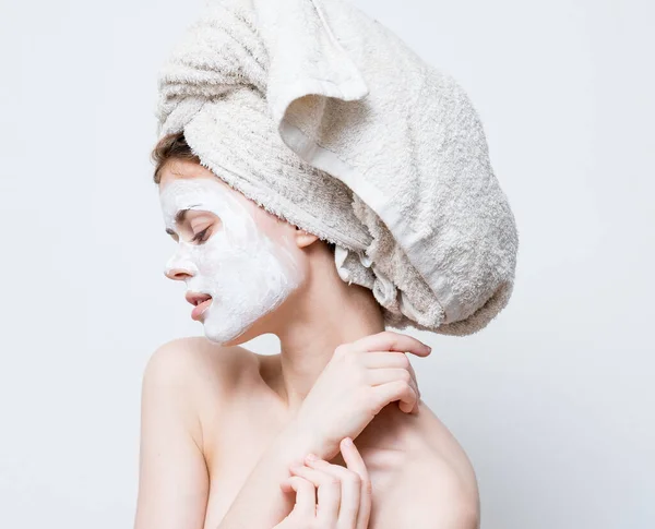 Une femme prend soin de son apparence et une serviette sur sa tête et une crème hydratante sur son visage — Photo