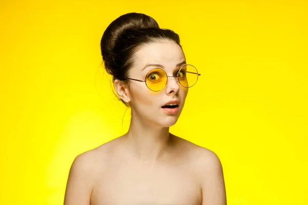 Kadının çıplak omuzları şaşkın, sarı gözlüklü, izole bir arka plan. — Stok fotoğraf