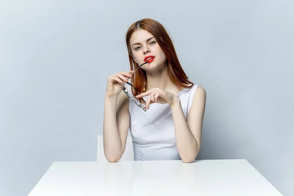 一个穿着白衣的女人坐在餐桌前，手里拿着他迷人的红唇模特的眼镜 — 图库照片