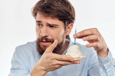 Sakallı bir adam arka planda hafif bir doğum gününde elinde pasta tutuyor.