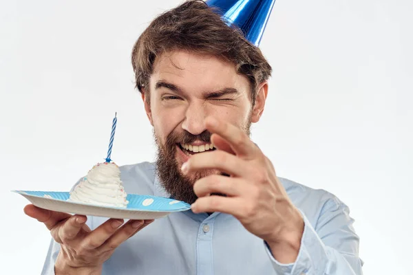 Un homme avec une assiette de gâteau et une chemise bleue sur un fond clair anniversaire fête chapeau d'entreprise — Photo