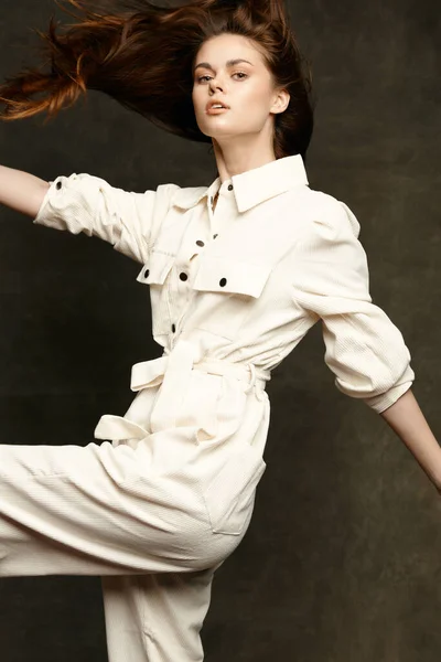 Energieke brunette gebaren met haar handen op een donkere achtergrond in een wit jumpsuit — Stockfoto