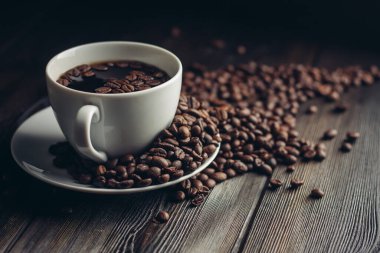 Ahşap bir masada mis kokulu kahve çekirdekleri ve çay tabağında sıcak bir içecek.