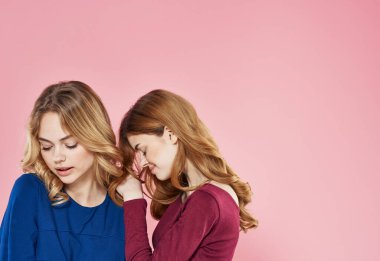 İki sevimli kız arkadaş, pembe arka planda sohbet ederek birbirlerine sarılıyorlar.