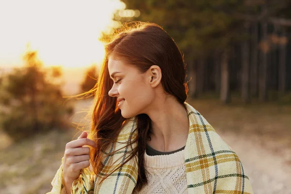 Happy woman with closed eyes at sunset near coniferous trees in the forest