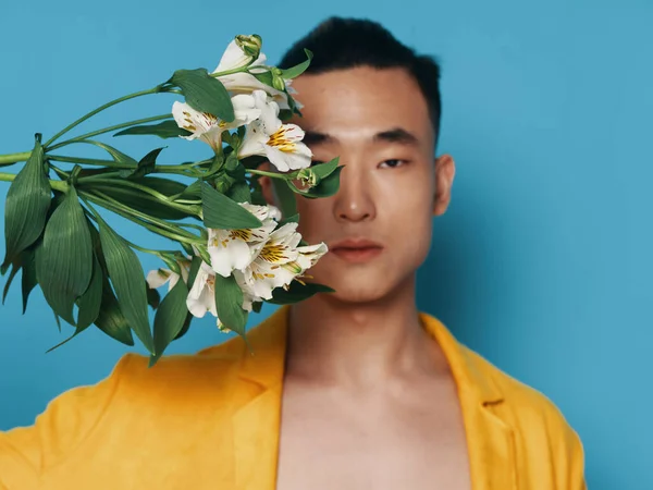 O cara segura um buquê de flores brancas e um casaco amarelo perto de seu rosto — Fotografia de Stock