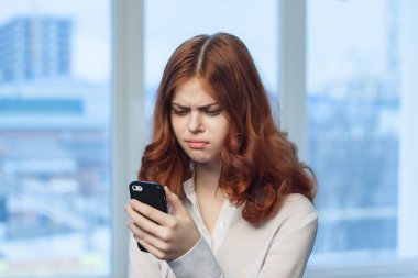 Elinde telefonu olan neşeli kızıl saçlı bir kadın resmi bir ofisten iletişim kuruyor.