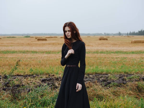 Eine schöne Frau im schwarzen Kleid geht im Herbst auf einem Feld in der Natur spazieren — Stockfoto