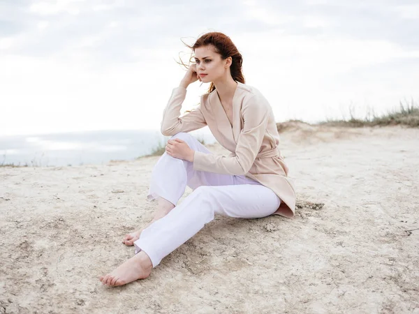 Uma mulher de roupas leves senta-se na areia perto do oceano na natureza — Fotografia de Stock
