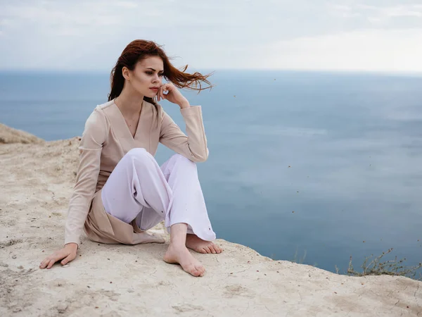 Une femme en vêtements légers est assise sur un rocher avec l'océan en arrière-plan — Photo