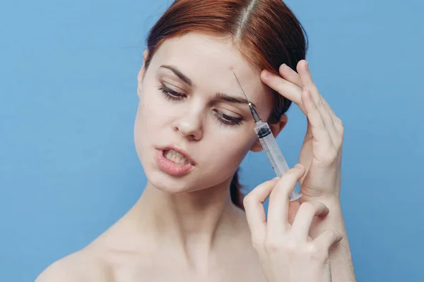 Femme fait une injection rajeunissante dans le visage sur un fond bleu et une seringue avec une aiguille botox — Photo