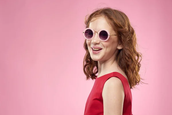 Dziewczyna z kręconymi włosami okulary słoneczne radość dzieciństwo różowy tło — Zdjęcie stockowe