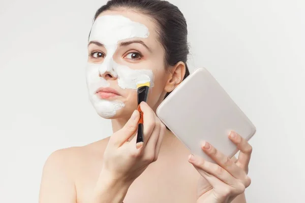 Hermosa morena desnuda hombros aplicando crema cepillo en el cuidado de la cara —  Fotos de Stock
