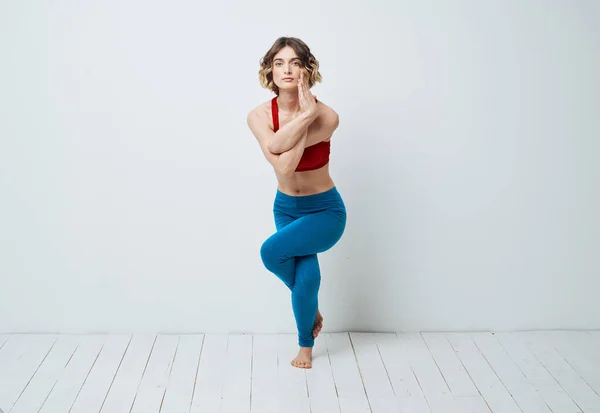 En kvinna i blå leggings gör övningar på en lätt bakgrund av yoga asana — Stockfoto