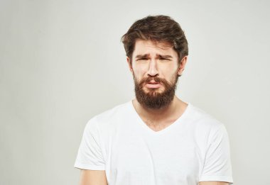 Beyaz tişörtlü, arka planda sakallı hoş bir adam üzgün bir yüz gördü.