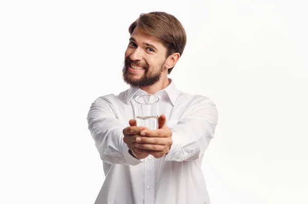 Vreugdevolle man steekt zijn hand uit met een glas water naar voren op een lichte achtergrond — Stockfoto