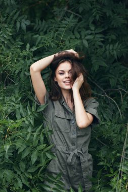 Dışarıdaki kadın elleriyle saçlarına dokunuyor ve ağaçlarla gülüyor.