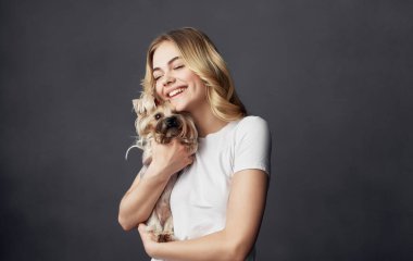 Beyaz tişörtlü neşeli bir kadın elinde küçük bir köpek evcil hayvanı tutuyor.