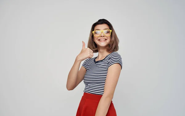 fashionable woman in glasses and in a striped t-shirt on a light background red skirt